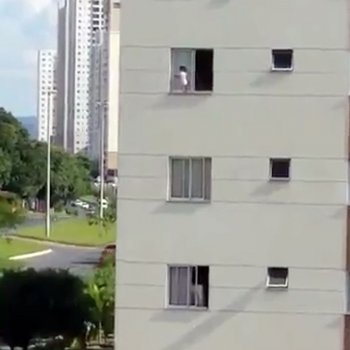Un bebé juega en la repisa de una ventana de un tercer piso
