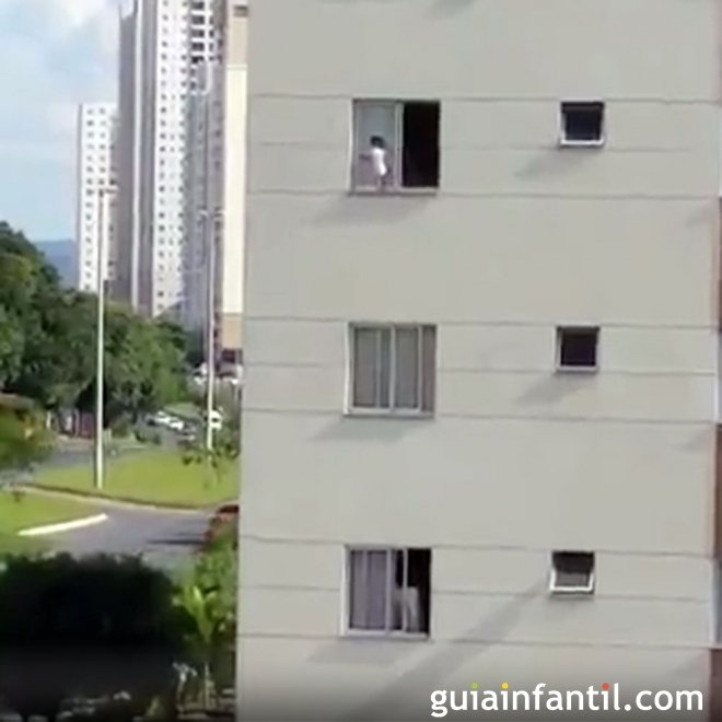 Un bebé juega en la repisa de una ventana de un tercer piso