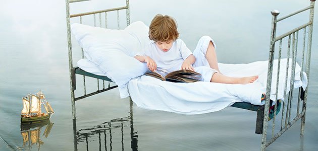 Fábulas infantiles Niño lee en cama sobre el mar
